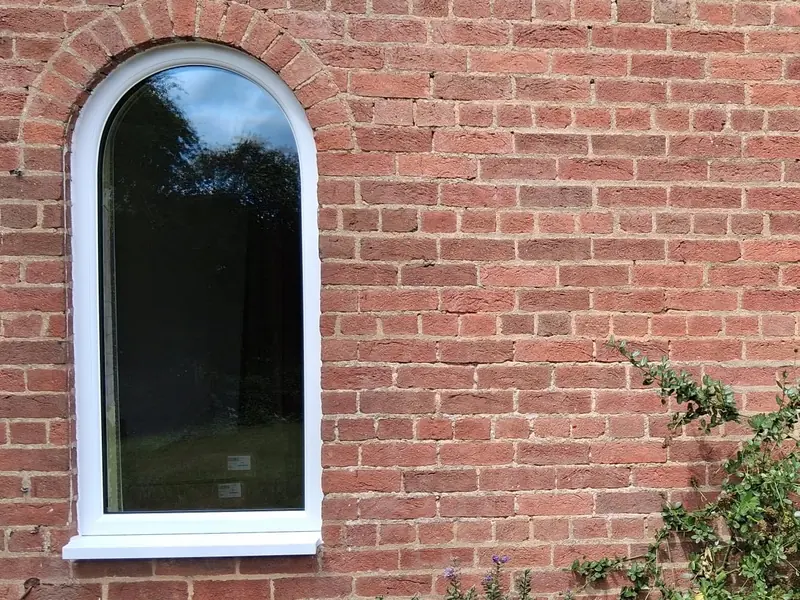 An arched white uPVC window set under a brick arch in a red-brick wall