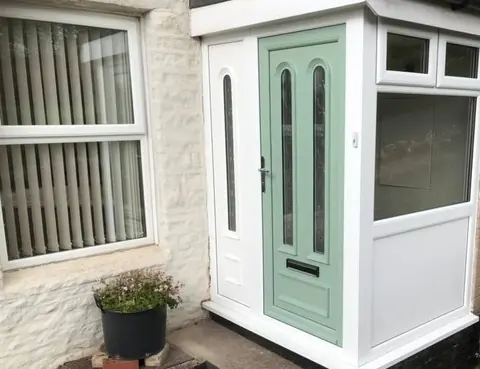 A pale green composite door in a white uPVC porch with glazed side panels, beside a white uPVC window