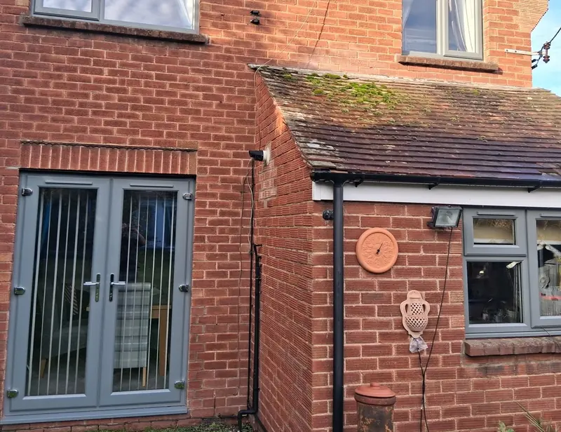 The back of a red-brick house with grey uPVC windows upstairs and down and matching grey French doors