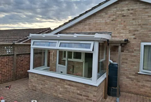 A white uPVC lean-to conservatory on a brick dwarf wall against the gable end of a bungalow