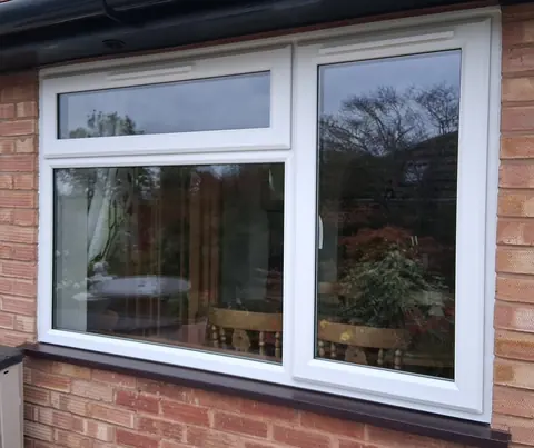 A white uPVC casement window with a top opener and a rosewood sill, fitted in a brick wall under black guttering