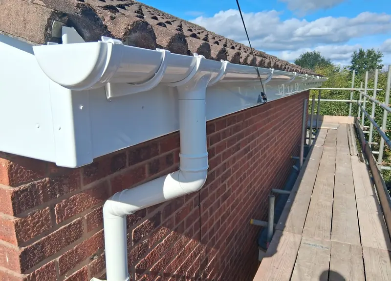 New white uPVC fascia, guttering and a downpipe on a brick house, seen from the scaffold