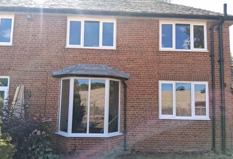 The back of a red-brick house fitted with new white uPVC windows upstairs and down, including a bay window with a lead roof